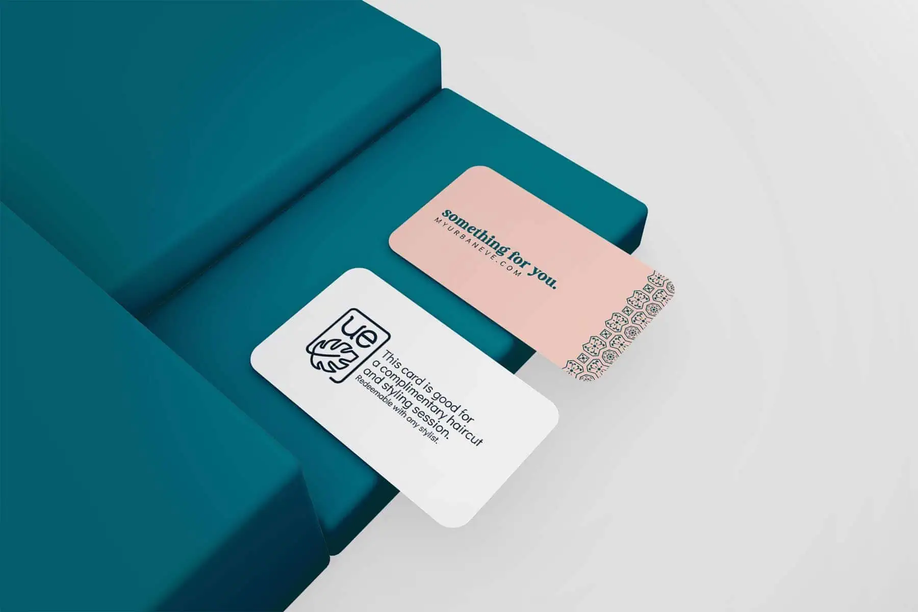 Two business cards placed on teal rectangular blocks. The upper card is pink and reads "something for you. urbaneve.com" with a decorative border. The lower card is white with a logo and text. MDT designs and prints a variety of marketing materials. - Market Design Team: Define. Structure. Expand.