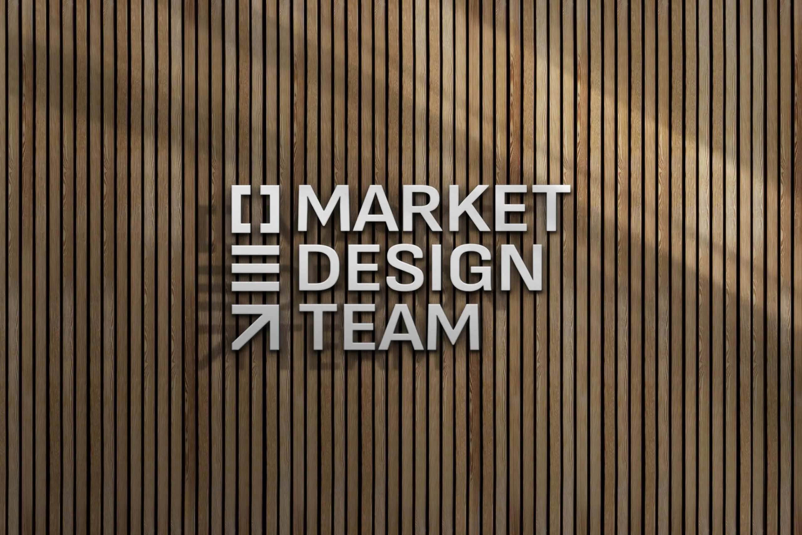 A vertical wooden plank wall serves as the background for a sign that reads "MARKET DESIGN TEAM" in modern, white, capital letters. The design includes horizontal, vertical, and diagonal line elements to the left of the text. - Market Design Team: Define. Structure. Expand.