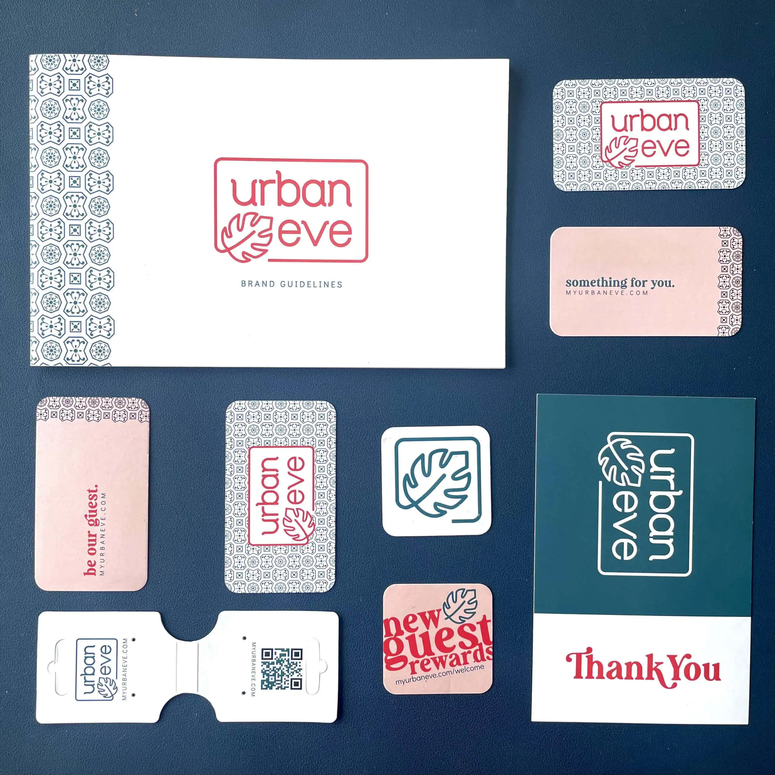 Various brand materials for "urban eve" are displayed on a dark blue surface. Items include cards, a brand guidelines booklet, stickers, and a USB containing QR codes and logos in pink, white, and teal colors. - Market Design Team: Define. Structure. Expand.