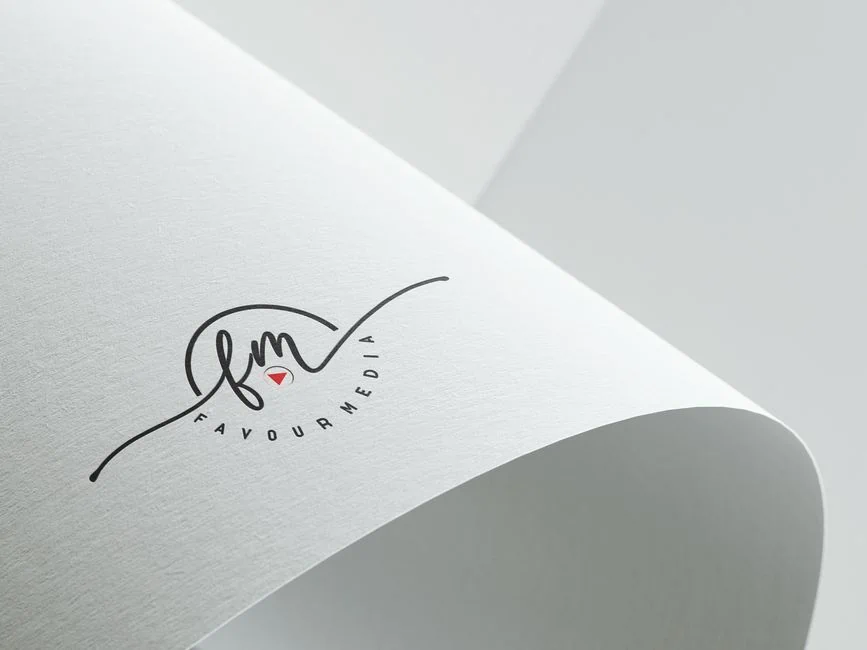 a close up of a white sheet of paper with a minimalist, professional logo showing “fm” in script, a small red triangle, and the text “favourmedia” printed underneath. the refined logo design highlights clean lines and subtle elegance. the paper is slightly curled at the edge—perfect for businesses or individuals in brazoria county seeking polished branding solutions. market design team: define. structure. expand.