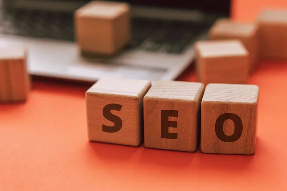 wooden blocks spelling “seo” are placed on an orange surface in front of a blurred laptop, illustrating the importance of local seo for businesses aiming to increase rankings in texas 77515. other wooden blocks are scattered in the background. market design team: define. structure. expand.